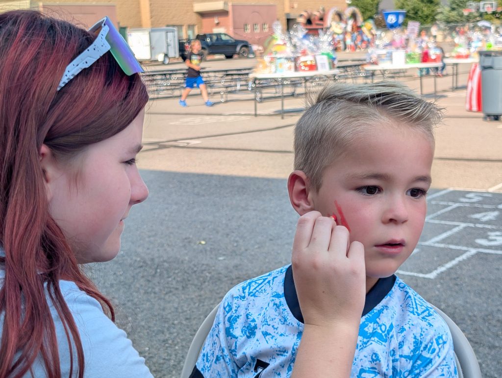 Girl painting a tiger scratch on a boy's face