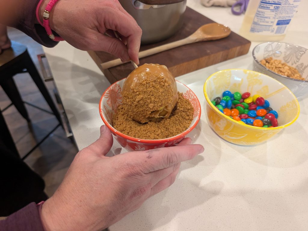 Covering a caramel apple in Biscoff cookie crumbs